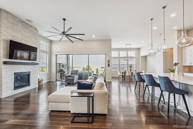 living room featuring sink, dark wood-type flooring, a fireplace, and ceiling fan with notable chandelier