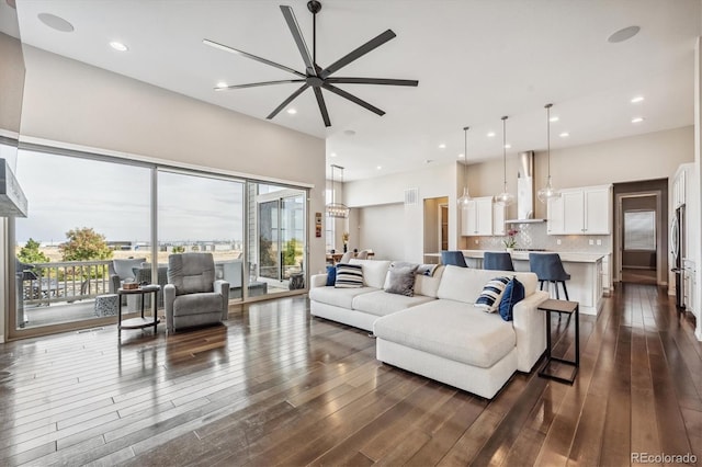 living room featuring a towering ceiling, dark wood-type flooring, and ceiling fan with notable chandelier