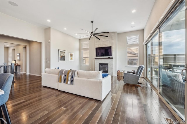 living room featuring a stone fireplace, dark hardwood / wood-style floors, and ceiling fan