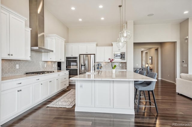 kitchen with white cabinets, an island with sink, appliances with stainless steel finishes, dark hardwood / wood-style floors, and wall chimney exhaust hood