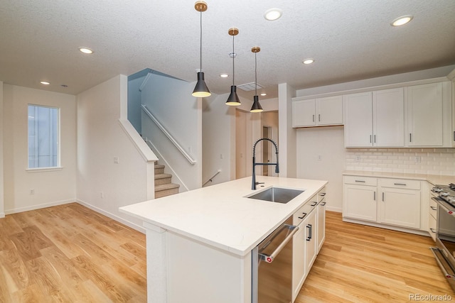 kitchen featuring light wood finished floors, decorative backsplash, dishwasher, light countertops, and a sink