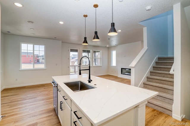 kitchen with pendant lighting, a glass covered fireplace, a sink, light stone countertops, and light wood-type flooring