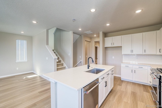 kitchen with a sink, light wood-style floors, appliances with stainless steel finishes, white cabinetry, and visible vents