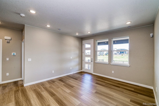 empty room with wood finished floors, a textured ceiling, and baseboards