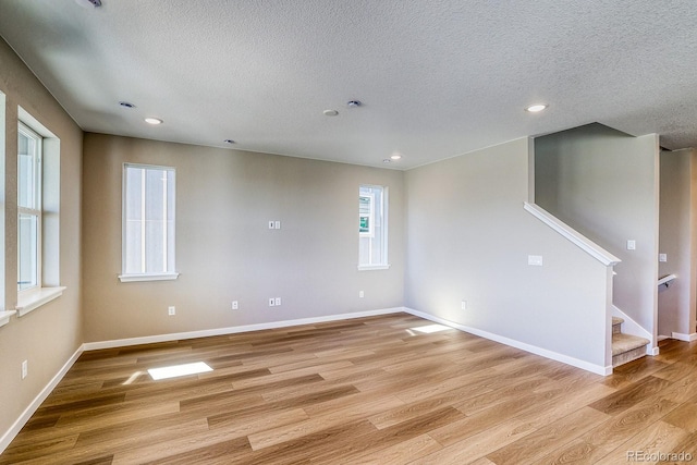 empty room featuring recessed lighting, stairway, baseboards, light wood-style flooring, and a textured ceiling