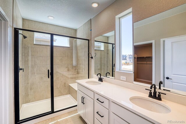 bathroom with a textured ceiling, a sink, a shower stall, and double vanity