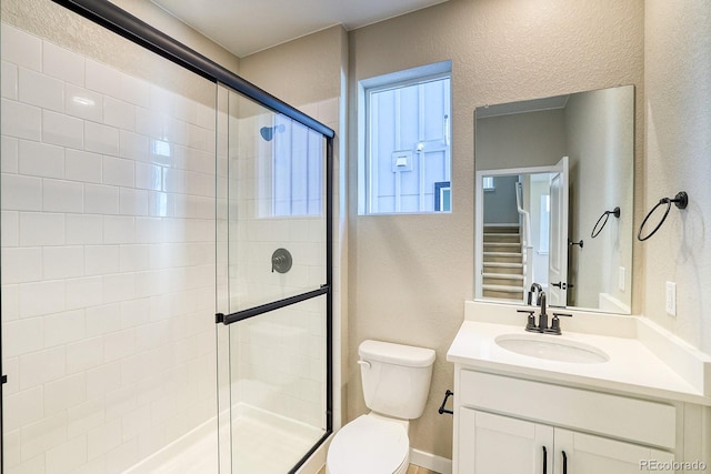 full bathroom featuring toilet, vanity, a textured wall, and a stall shower