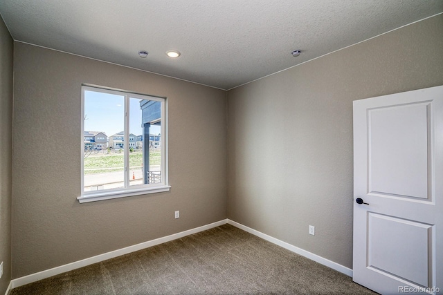 spare room with dark colored carpet, baseboards, and a textured ceiling