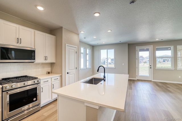 kitchen with a textured ceiling, a sink, light wood-style floors, decorative backsplash, and appliances with stainless steel finishes