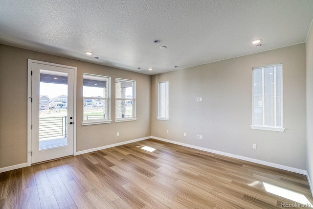 spare room with light wood-style flooring, baseboards, and a textured ceiling