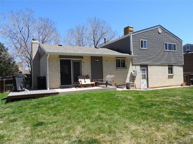 back of house with a chimney, a wooden deck, a yard, roof with shingles, and brick siding
