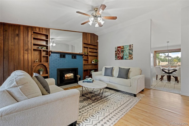 7563 Lamar Ct, Arvada, CO 80003 - living area featuring a ceiling fan, light wood-style floors, built in shelves, a brick fireplace, and wood walls