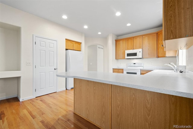 kitchen featuring sink, light wood-type flooring, white appliances, and kitchen peninsula