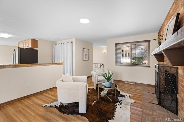 sitting room featuring light wood-type flooring, visible vents, baseboards, and a brick fireplace