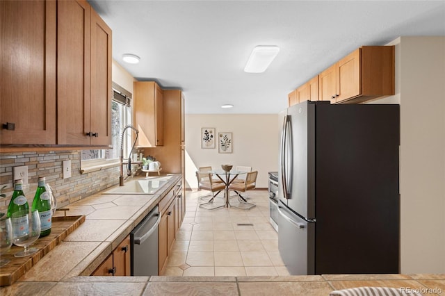 kitchen with tile countertops, light tile patterned floors, a sink, appliances with stainless steel finishes, and backsplash