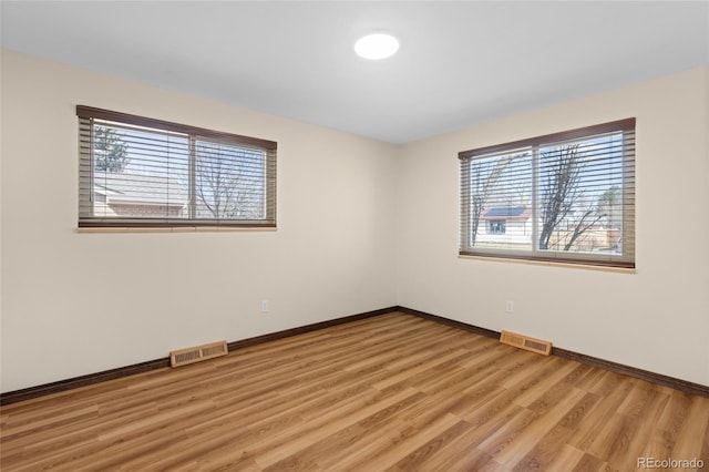 empty room with visible vents, light wood-type flooring, and baseboards