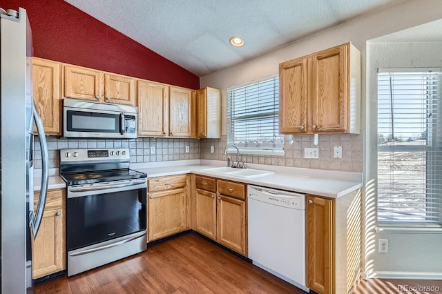 kitchen with appliances with stainless steel finishes, hardwood / wood-style floors, lofted ceiling, sink, and backsplash