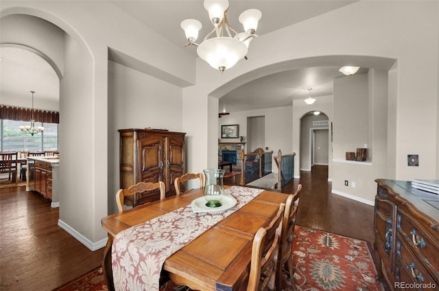 15616 Soo Line Way, Monument, CO 80132 - dining room featuring a chandelier, arched walkways, dark wood finished floors, a stone fireplace, and baseboards