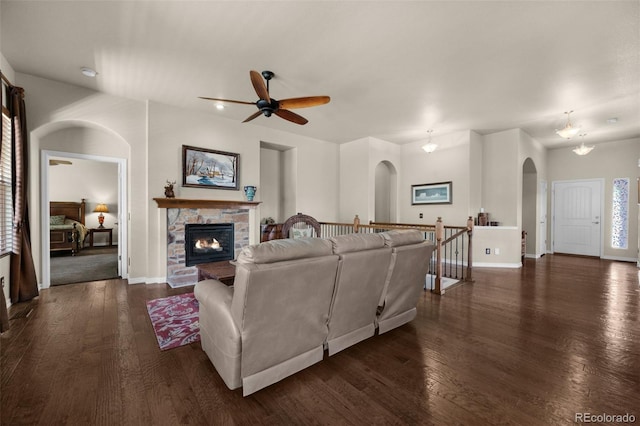 15616 Soo Line Way, Monument, CO 80132 - living room with arched walkways, dark wood-type flooring, a stone fireplace, ceiling fan, and baseboards