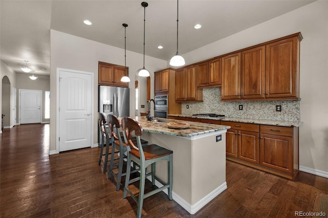 15616 Soo Line Way, Monument, CO 80132 - kitchen featuring arched walkways, brown cabinetry, dark wood-type flooring, decorative backsplash, and light stone countertops