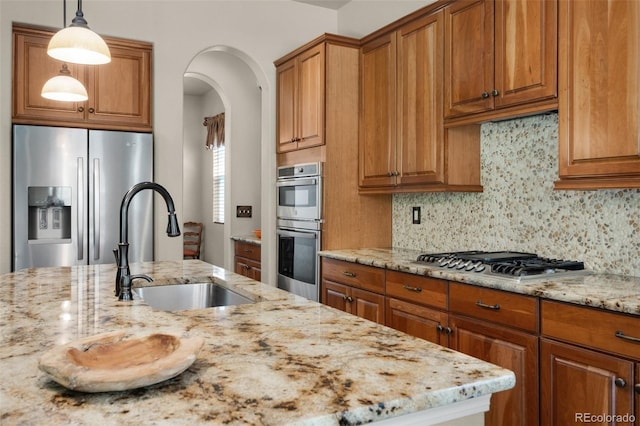 15616 Soo Line Way, Monument, CO 80132 - kitchen featuring stainless steel appliances, a sink, brown cabinetry, light stone counters, and decorative backsplash