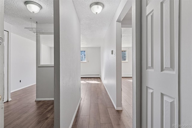 hall featuring a baseboard radiator, a textured ceiling, baseboards, and wood finished floors