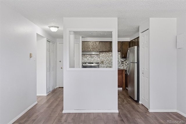 interior space featuring under cabinet range hood, decorative backsplash, stainless steel appliances, and wood finished floors