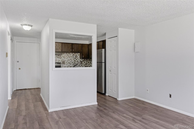 interior space with baseboards, wood finished floors, freestanding refrigerator, dark brown cabinets, and backsplash