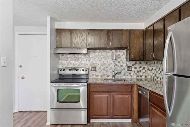 kitchen featuring backsplash, light wood-style flooring, appliances with stainless steel finishes, a sink, and under cabinet range hood