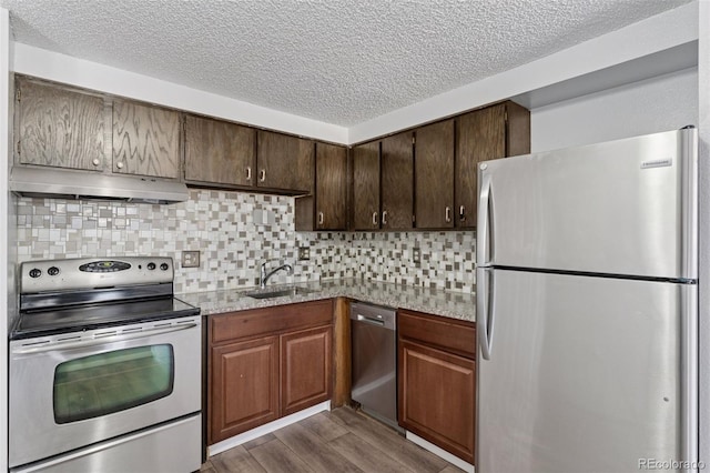 kitchen with decorative backsplash, appliances with stainless steel finishes, dark wood-type flooring, under cabinet range hood, and a sink