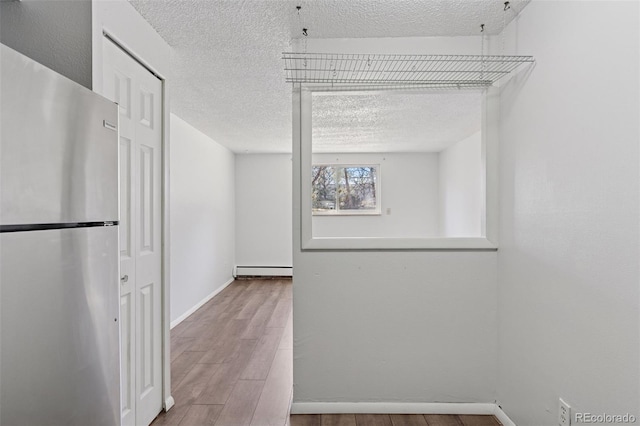 interior space featuring a textured ceiling, baseboard heating, wood finished floors, and baseboards