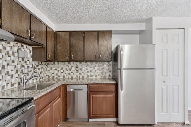 kitchen featuring light stone counters, a sink, dark brown cabinets, appliances with stainless steel finishes, and tasteful backsplash