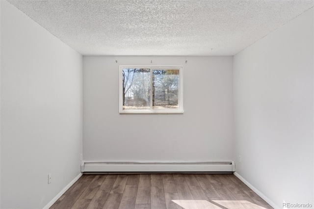 unfurnished room with a baseboard heating unit, a textured ceiling, wood finished floors, and baseboards