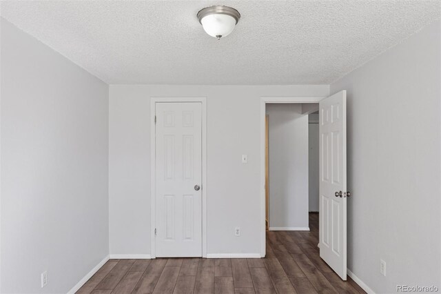 unfurnished bedroom with a textured ceiling, baseboards, and wood finished floors