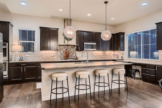 kitchen featuring pendant lighting, an island with sink, stainless steel appliances, and dark hardwood / wood-style floors