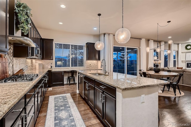 kitchen with tasteful backsplash, a kitchen island with sink, dark wood-type flooring, sink, and pendant lighting