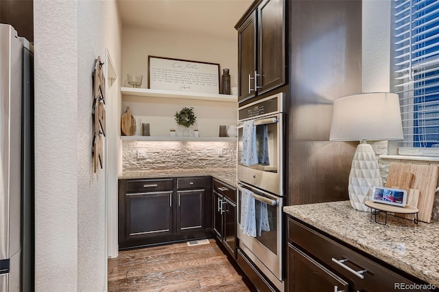 kitchen featuring dark wood-type flooring, appliances with stainless steel finishes, tasteful backsplash, dark brown cabinets, and light stone counters