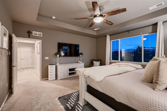 bedroom featuring ceiling fan, light colored carpet, and a tray ceiling