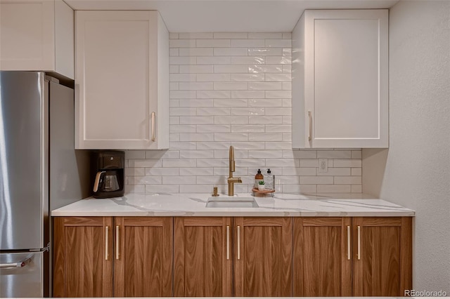 kitchen featuring stainless steel fridge, light stone countertops, white cabinetry, and backsplash