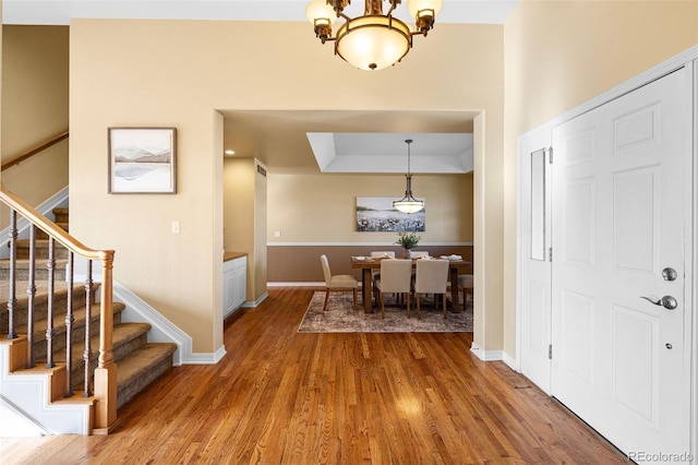 entryway with stairway, wood finished floors, baseboards, a raised ceiling, and a notable chandelier