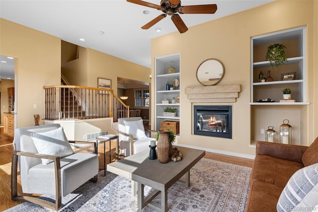 living room featuring visible vents, built in shelves, a glass covered fireplace, wood finished floors, and stairway