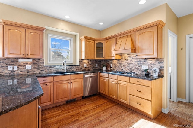 kitchen featuring premium range hood, a sink, decorative backsplash, light wood-style floors, and appliances with stainless steel finishes