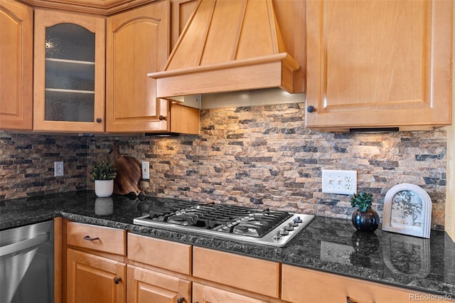 kitchen featuring backsplash, glass insert cabinets, custom range hood, dark stone countertops, and stainless steel appliances