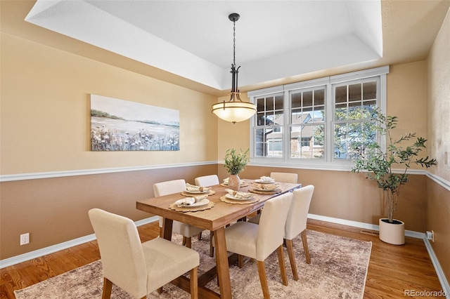 dining room featuring a raised ceiling, wood finished floors, and baseboards