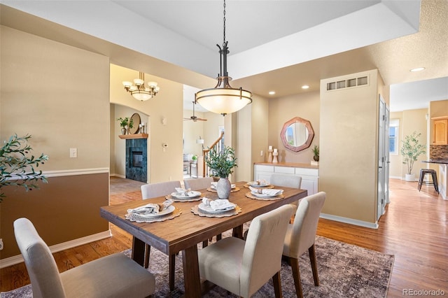 dining area with a tiled fireplace, baseboards, visible vents, and light wood finished floors