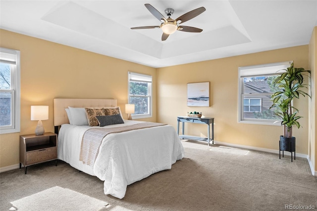 carpeted bedroom with ceiling fan, a raised ceiling, and baseboards