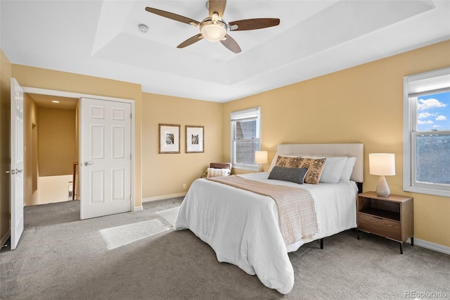 carpeted bedroom featuring a tray ceiling, baseboards, and ceiling fan