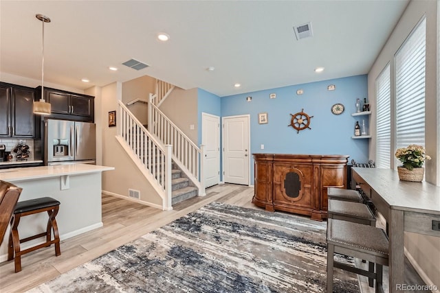 kitchen featuring light hardwood / wood-style flooring, hanging light fixtures, stainless steel refrigerator with ice dispenser, dark brown cabinets, and a breakfast bar