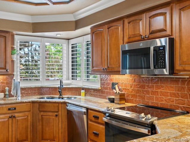 10954 W 100th Way, Broomfield, CO 80021 - kitchen featuring appliances with stainless steel finishes, brown cabinets, light stone counters, decorative backsplash, and crown molding