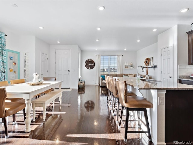 kitchen featuring tasteful backsplash, an island with sink, sink, a breakfast bar area, and dark wood-type flooring